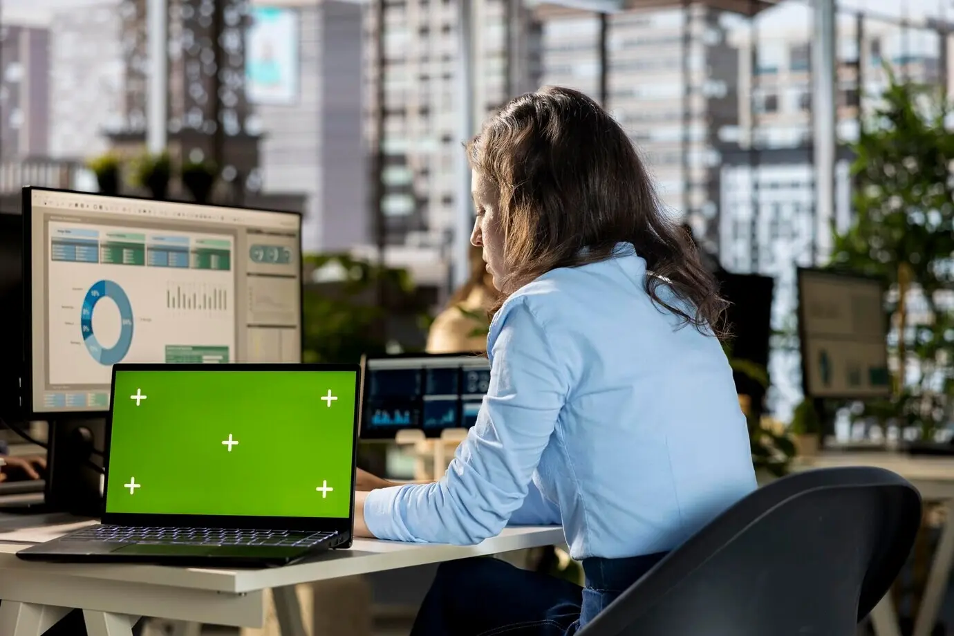 Молодая женщина-аналитик работает над онлайн-отчётами рядом с зелёным экраном.